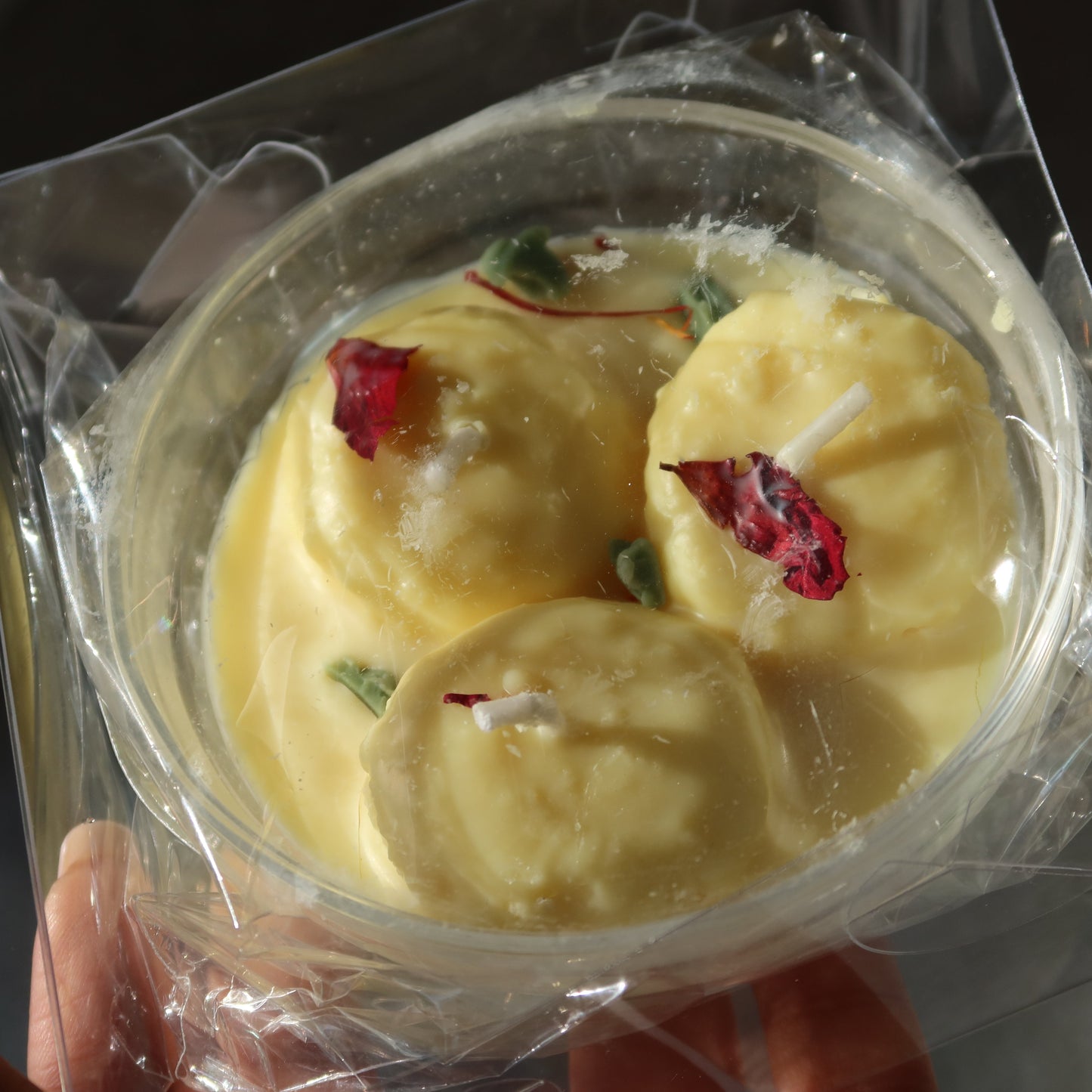 Three yellow spherical treats with red and green elements in a clear plastic container held by a person.